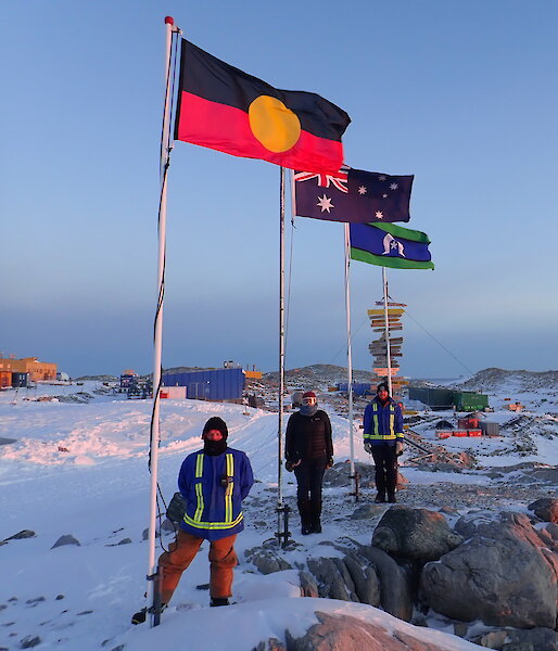 Three people standing under a flag pole with flag flying