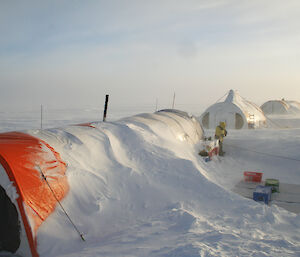 A large orange and white ice core drilling tent half buried by snow