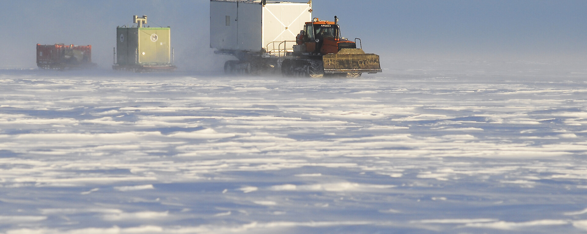 A large tractor towing container sleds across the ice