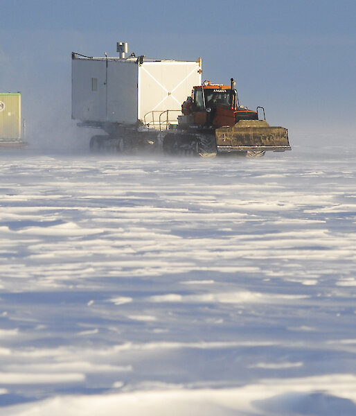 A large tractor towing container sleds across the ice