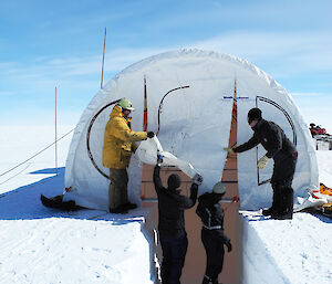 Four Antarctic expeditioners setting up a large white drilling tent on a clear day.