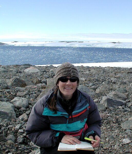 A researcher in a rocky Antarctic landscape taking notes in a field journal.