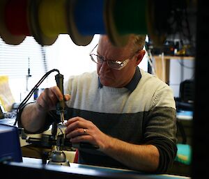 A man in an electronics workshop operating a soldering iron.