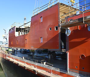 A superstructure block being craned into place above the watertight hull.