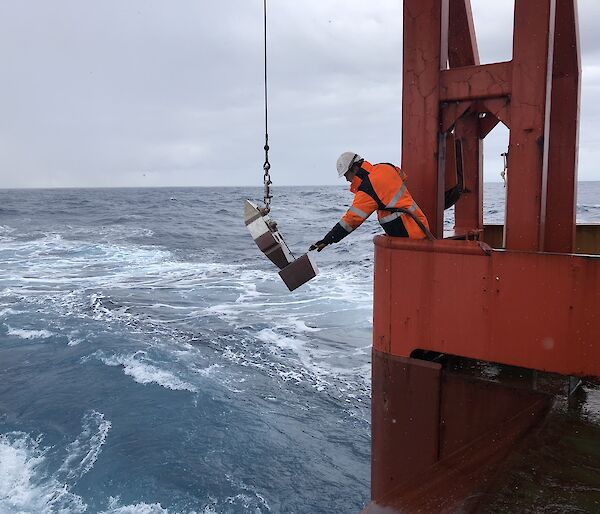 An expeditioner lowers a plankton sampling device into the Southern Ocean from the trawl deck of the Aurora Australis.