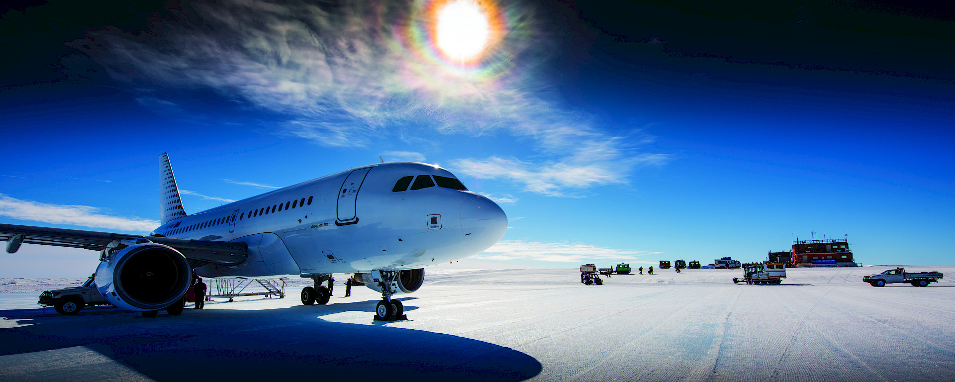 The sun shining brightly through the clouds over a white jet aircraft on an ice runway in Antarctica