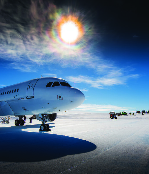 The sun shining brightly through the clouds over a white jet aircraft on an ice runway in Antarctica