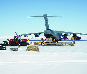 Various vehicles surrounding a large military cargo aircraft on the ice in Antarctica