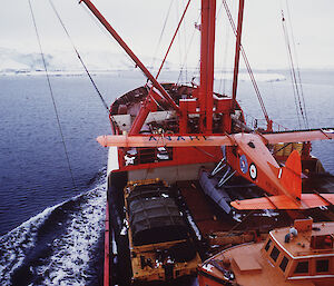 An orange aircraft on the deck of a ship with the Antarctic coast in the background