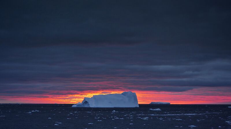 An iceberg against a pink sunset.