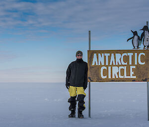 Man stands next to Antarctic Circle sign