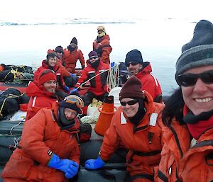 Science team in their orange suits sit by the water, preparing for boat trip