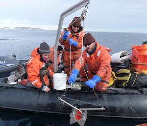 Three scientists lean over the side of the inflatable boat collecting marine samples