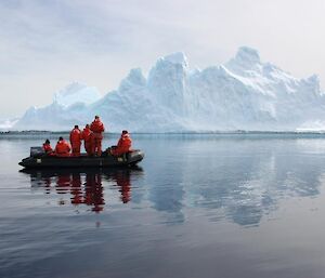Expeditioners in an inflatable boat gaze at a huge ice berg.