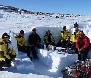 Expeditioners are sitting around a table cut out of ice eating and drinking.