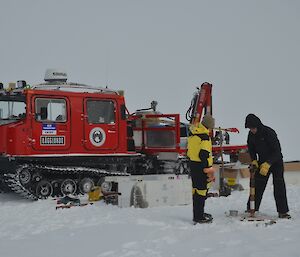 Two people collecting core samples with large red vehicle behind