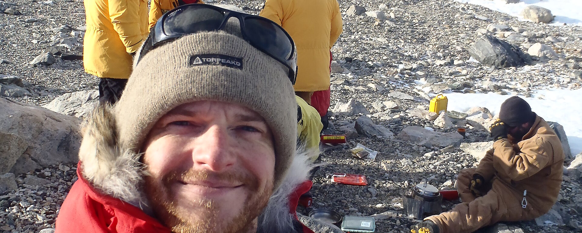 Mike Kennard, expedition mechanic, on location with dinner being prepared in the background