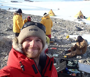 Mike Kennard, expedition mechanic, on location with dinner being prepared in the background