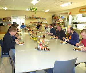 Small group of expeditioners eat at a table in the mess.