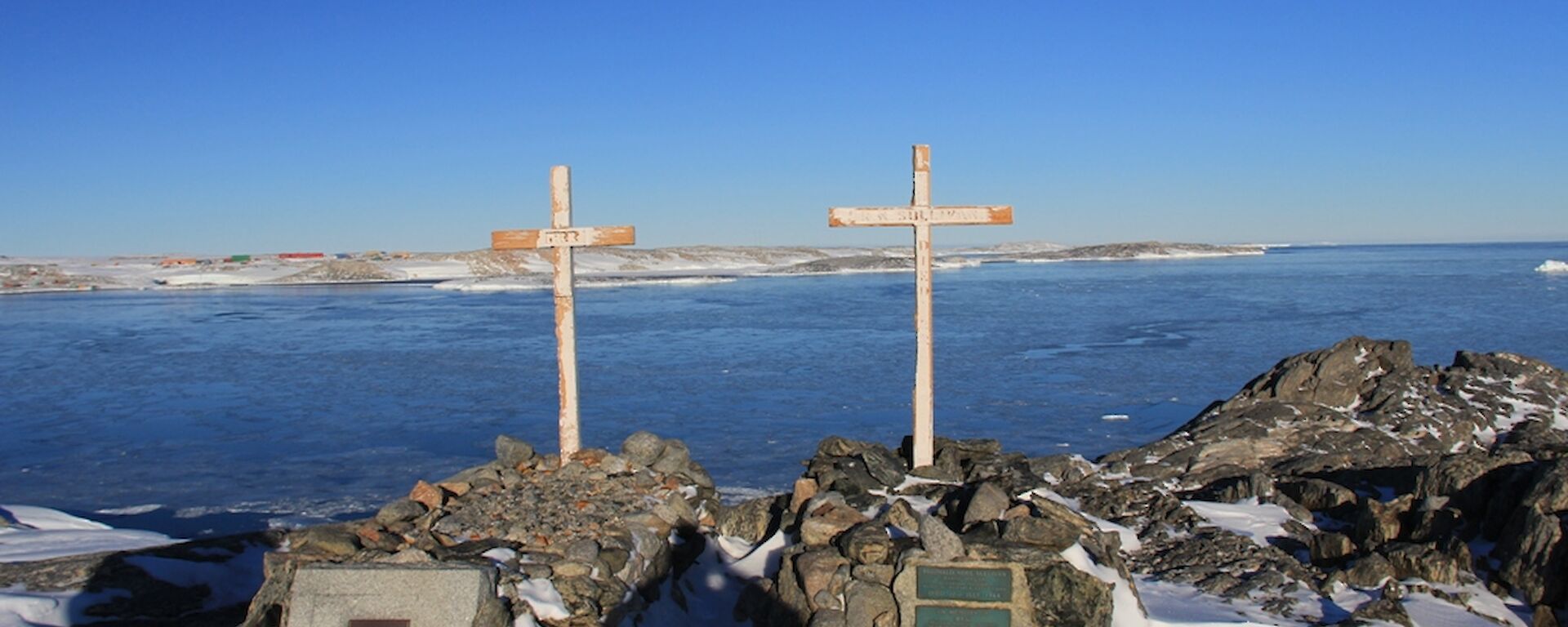 Wilkes graves — original crosses and plaques on rocky outcrops with ice in the background