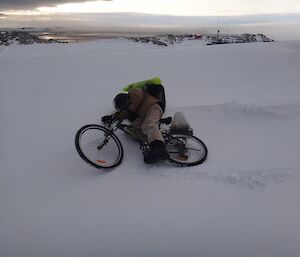 Mike on his bike, resting in the snow appearing to have fallen over