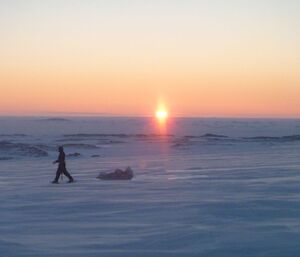 Sunset on the coast with an expeditioner walking across the ice