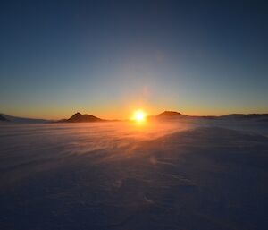 Sunset at Browning with very bright sun descending behind a horizon in between peaks