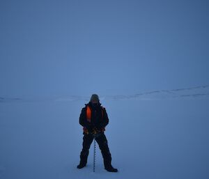 Jason drilling a core to test the depth and quality of the sea ice surrounded by nothing but white land and sky
