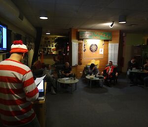 Photo of quiz night participants from behind the quiz host in red and white striped hat and shirt