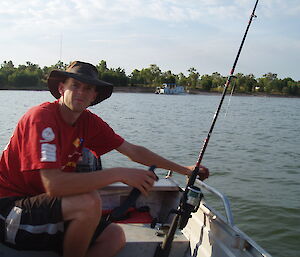 Mike Kennard poses in a tin fishing boat with fishing rod (in Australia)