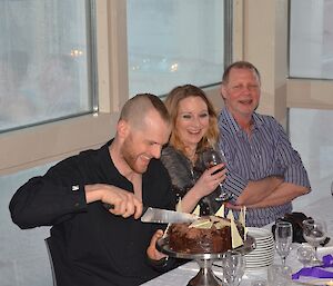Mike cutting his birthday cake with Bri and Andy looking on