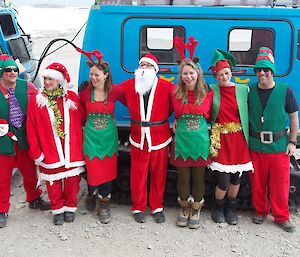 Expeditioners dressed as Santa, Mrs Claus and elves pose in front of Hagglund.