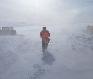 Blowing snow over Casey station blurs out the figure of a male expeditioner at the centre of the photo