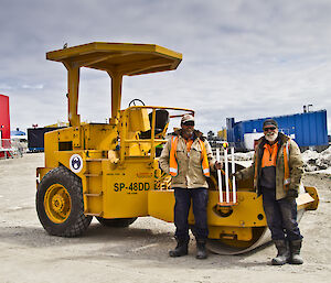 Two expeditioners posing with wickets on hand and roller in the background