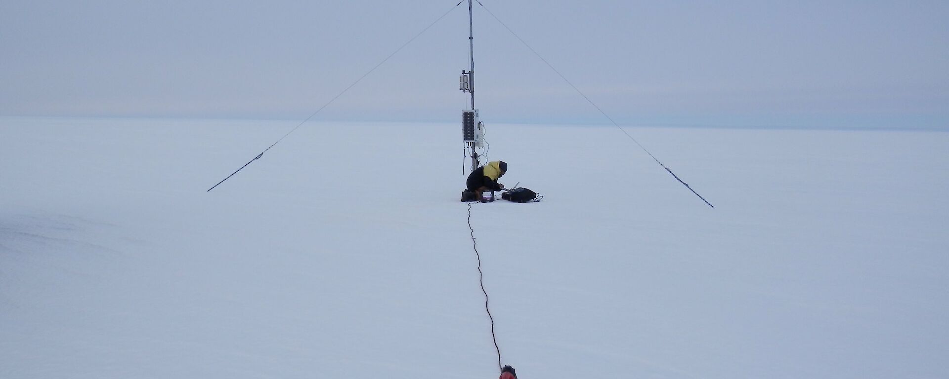 Expeditioner leans over laptop in snow underneath a weather tower (AWS)