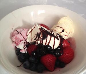 A bowl of ice cream with cream, strawberries and blue berries