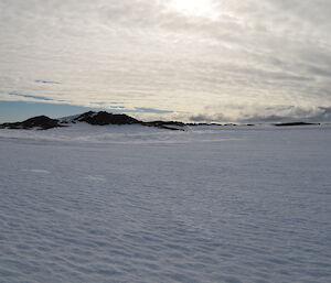 Picture of snow covered terrain with a few rocky peaks in the background.
