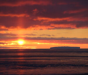 Sunset over the ocean, an iceberg in the distance. Different shads of red and pink