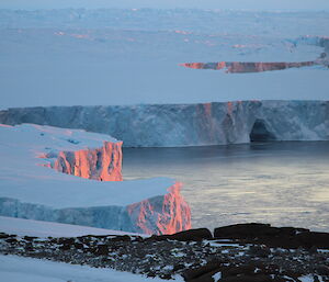Glacier cliffs meeting the ocean with a tinge of pink from the setting sun