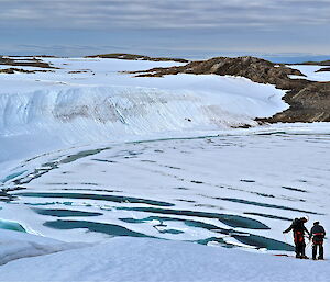 A shot over looking O'Briens Bay with a large ice cliff in the background and two people setting up gear in the foreground