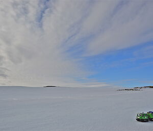 A snowy terrain with a few rocky peaks and a green hagglund in the foreground