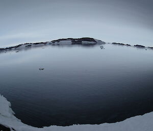 A fish eye view of a bay with a reflection of the dark sky off the still water