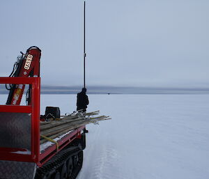 Endless flat white snow and ice terrain with Doug checking a cane post, on the right hand bottom conner is the back tray of a Hägglunds with new canes loaded