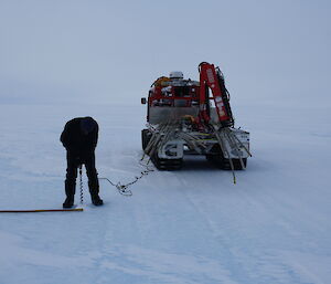 Drilling a hole in the ice for the cane with the red Hägglunds in the background