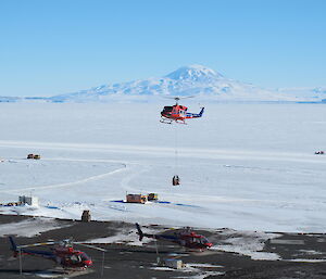 A Huey helicopter lifting cargo with a tall mountain in the background