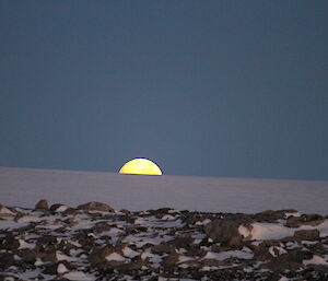 Moon in the horizon rising from snowy and rocky terrain