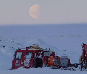 Large moon in the sky with a red Hägglunds in the foreground