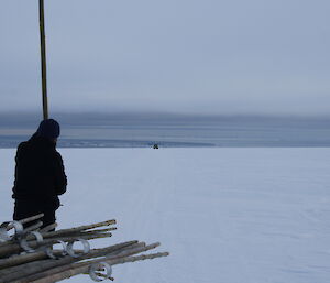 Cloudy and white flat snowy terrain, with an expeditioner standing with a cane in the foreground