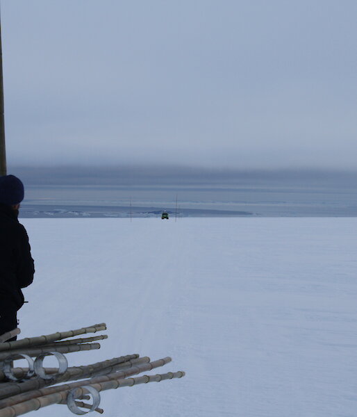 Cloudy and white flat snowy terrain, with an expeditioner standing with a cane in the foreground