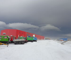 Big red shed on the corner background with blowing snow with dark low clouds and Hägglunds in the foreground